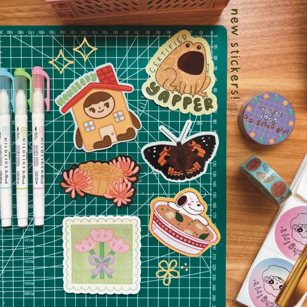 Collection of stickers and stationery items on a cutting mat with a wooden surface.